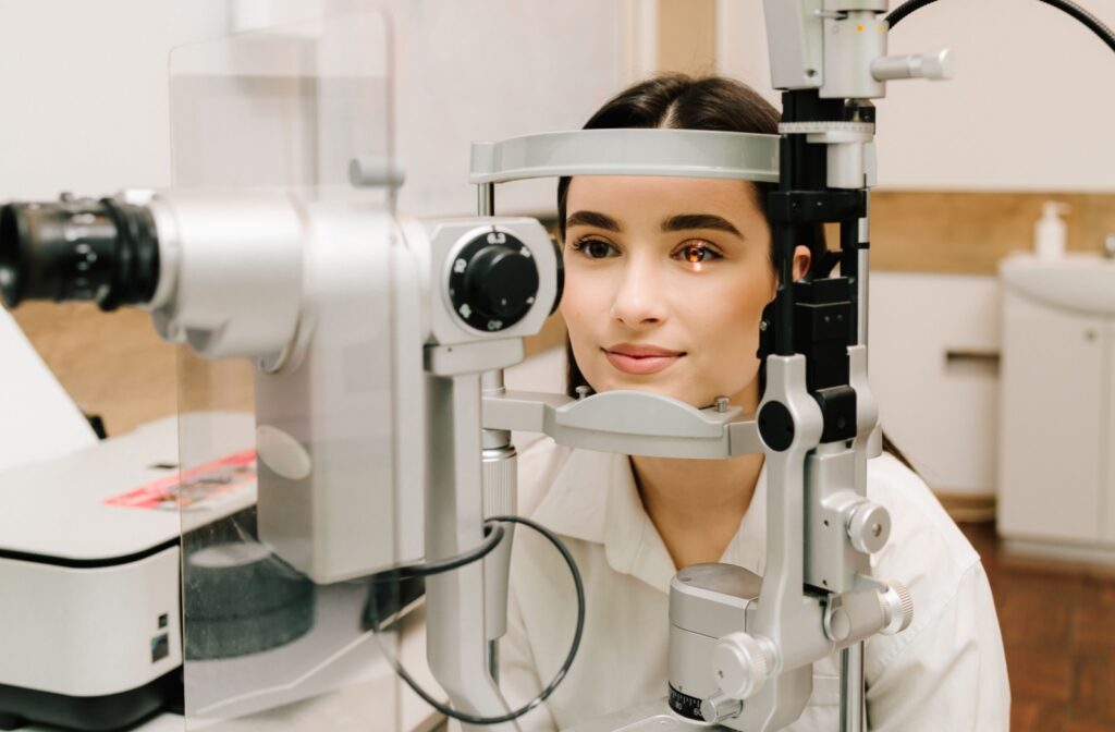 A young adult sits patiently as they undergo a slit lamp examination during their eye exam.